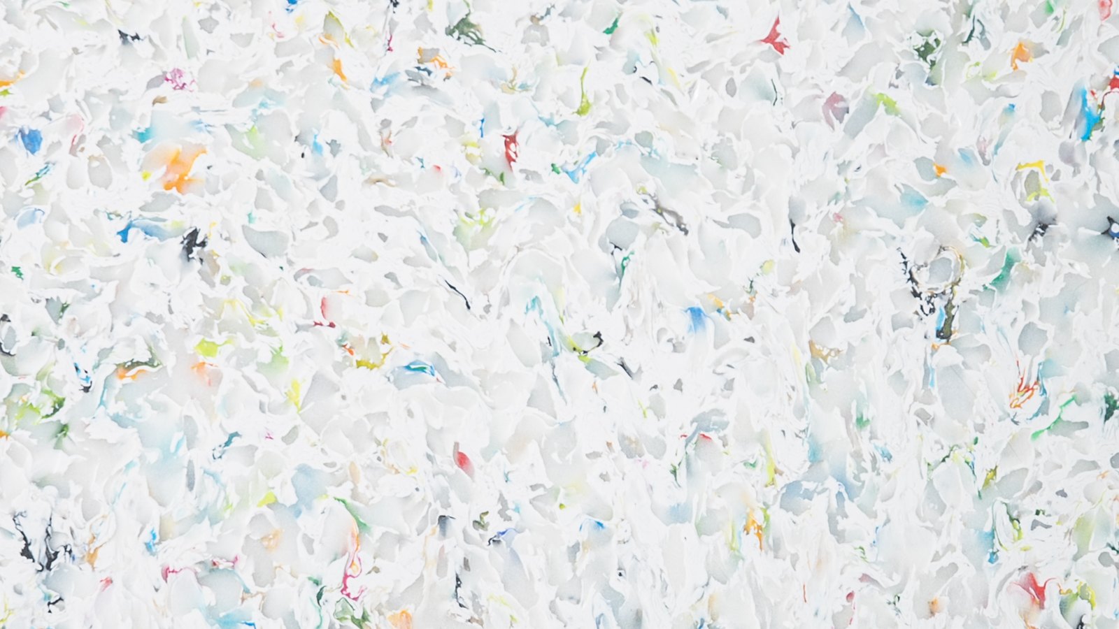 再生プラスチック板の表面。白を地に、青・赤・黒などの細かな破片が混ざり合っている