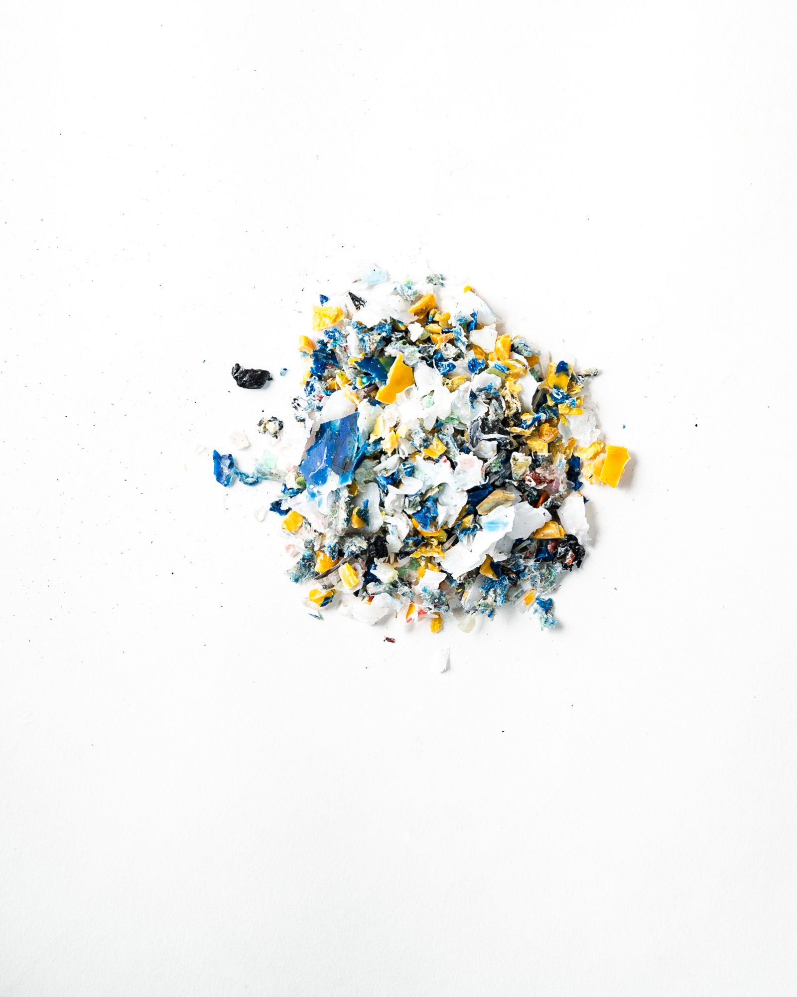 粉砕された廃プラスチックのチップ。白を地に青と黄の破片が混ざっている